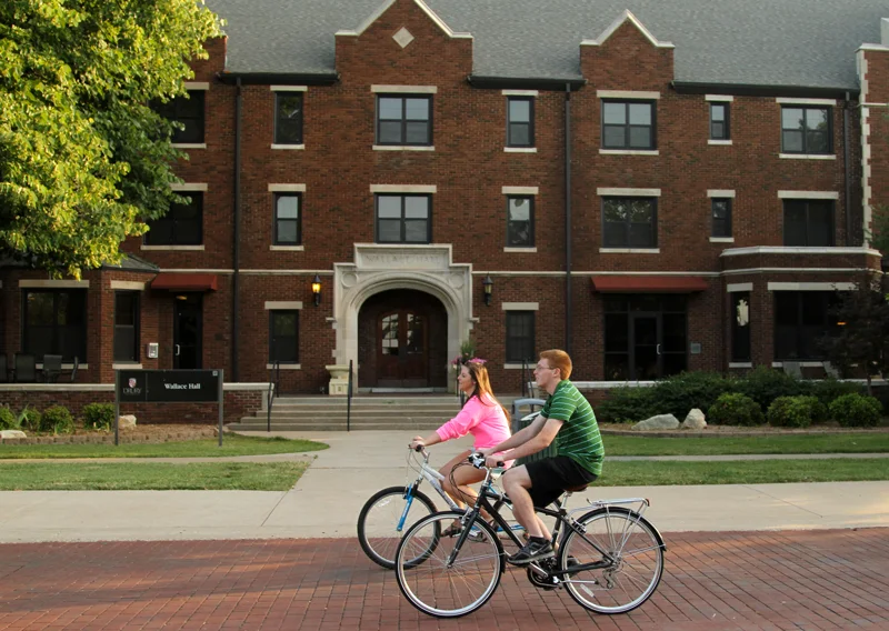 Students riding bicycles outside a college campus brick building