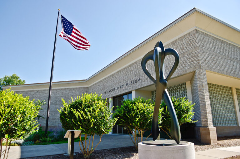 Front of Springfield Art Museum in Springfield Missouri. In front of the entrance stands an American flag and a large sculpture.