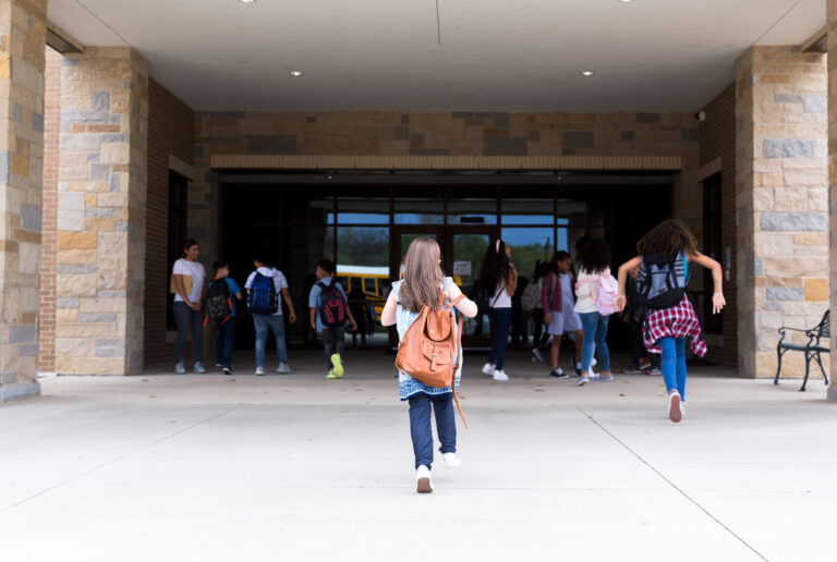 Rear view of elementary students walking into the school building