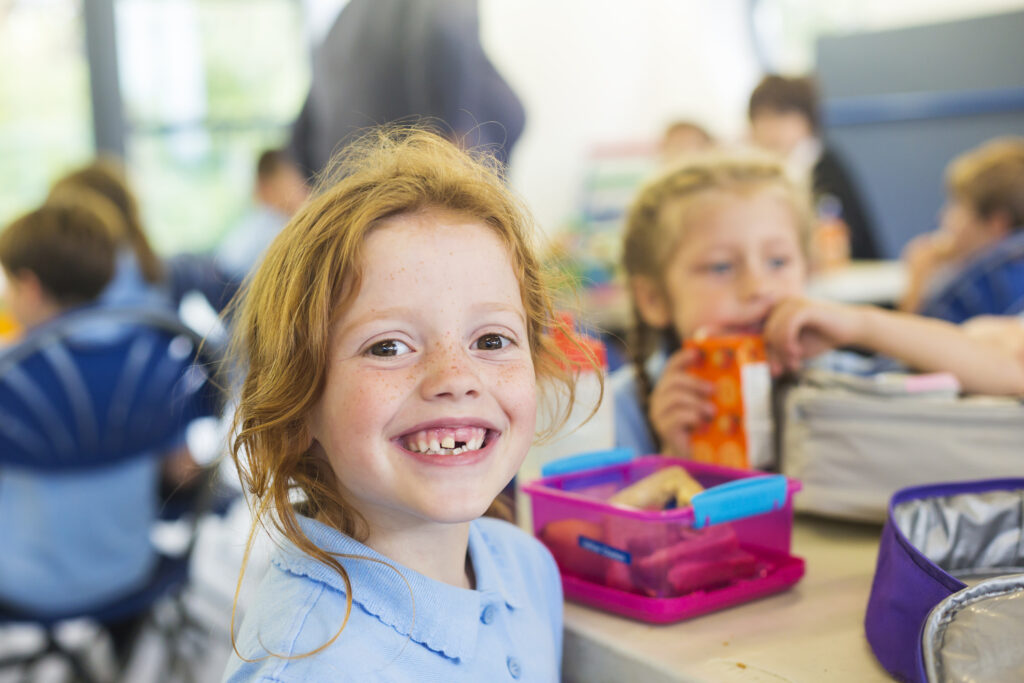 Smiling school students in uniform missing a tooth with a healthy sandwich for lunch