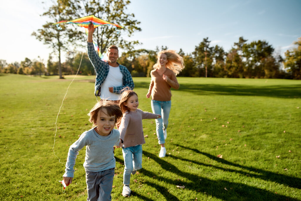 Cheerful parents with two kids fly a kite in a local park in Springfield Missouri on a sunny day.