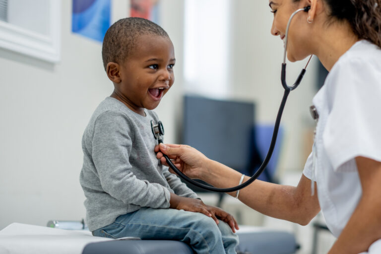 A happy young boy sits on an exam table during his visit with a pediatrician.